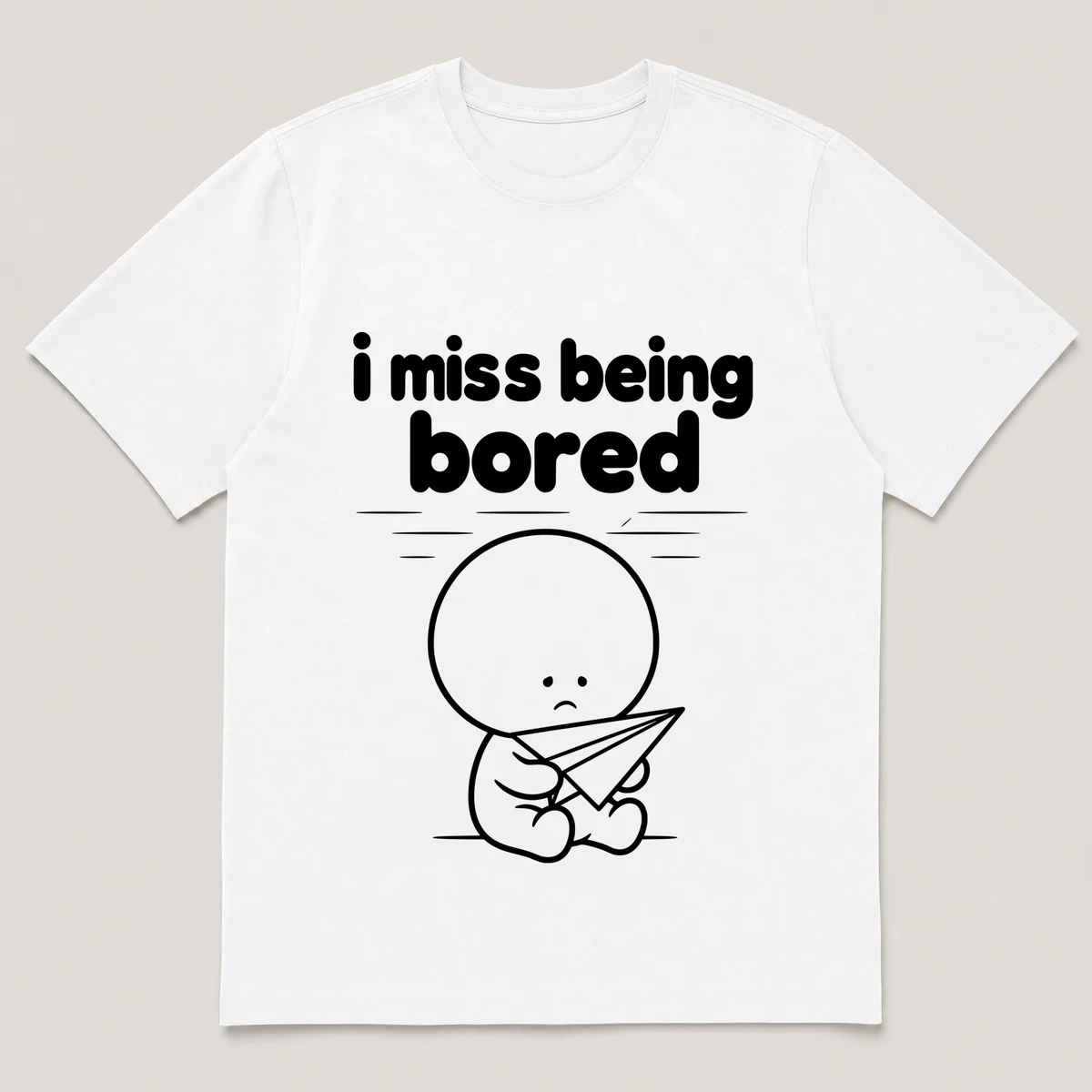 lonely boi tee: a small sad cartoon boy hugging a paper airplane drifting across a ceiling, with the words i miss being bored above him, White front view