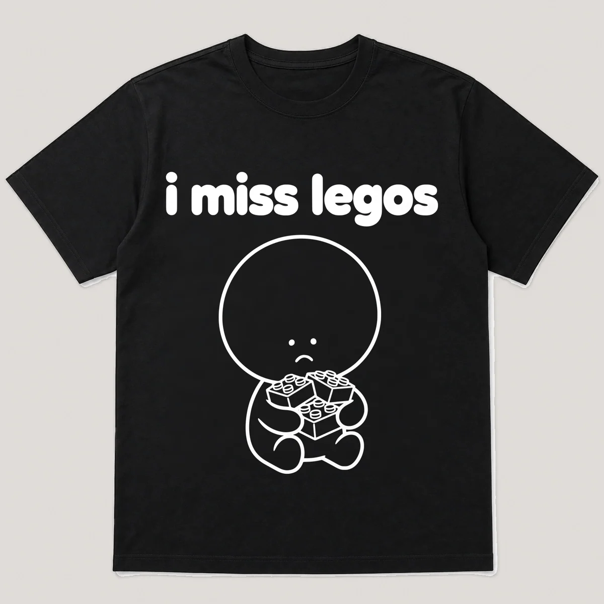 lonely boi tee: a small sad cartoon boy hugging a pile of small colorful building bricks, with the words i miss legos above him, Black front view
