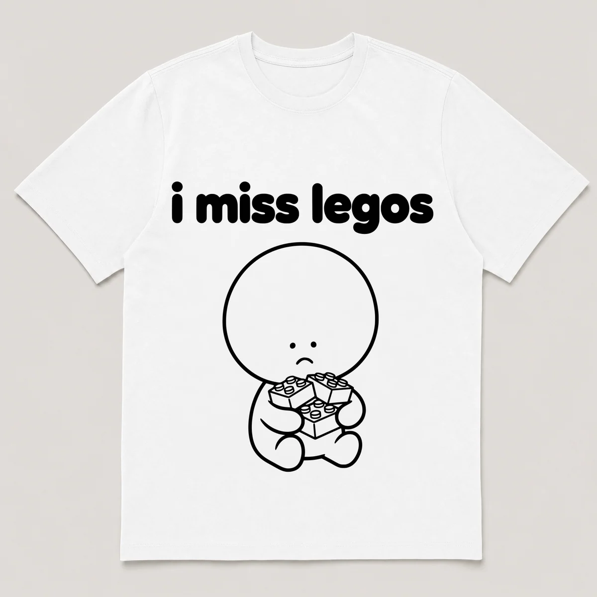 lonely boi tee: a small sad cartoon boy hugging a pile of small colorful building bricks, with the words i miss legos above him, White front view