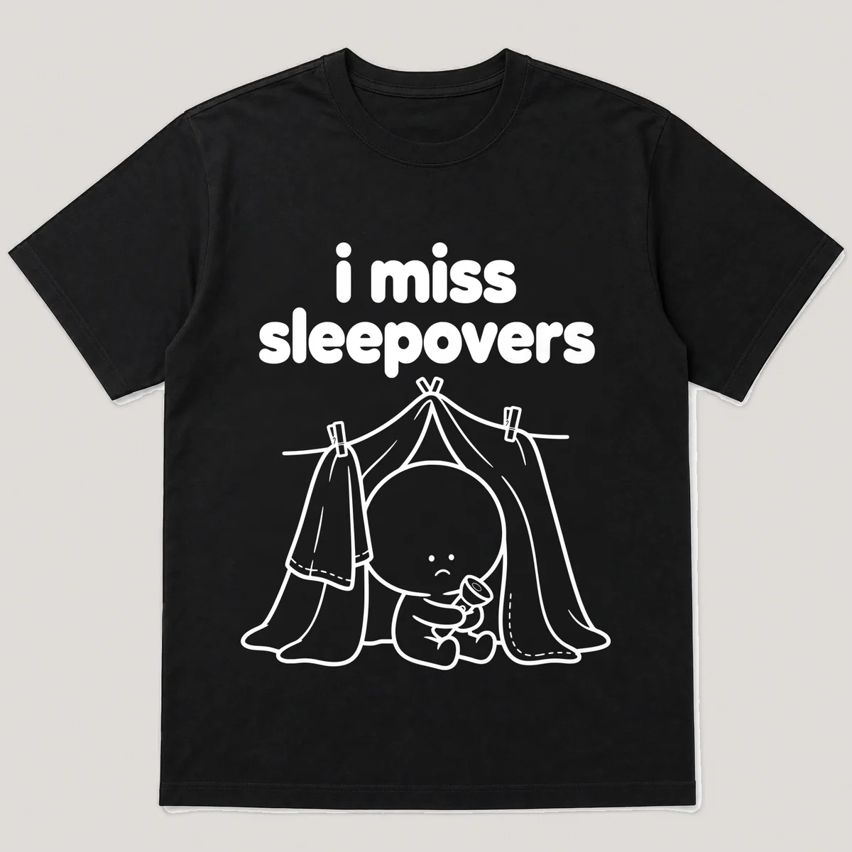 lonely boi tee: a small sad cartoon boy hugging a blanket fort with a flashlight, with the words i miss sleepovers above him, Black front view