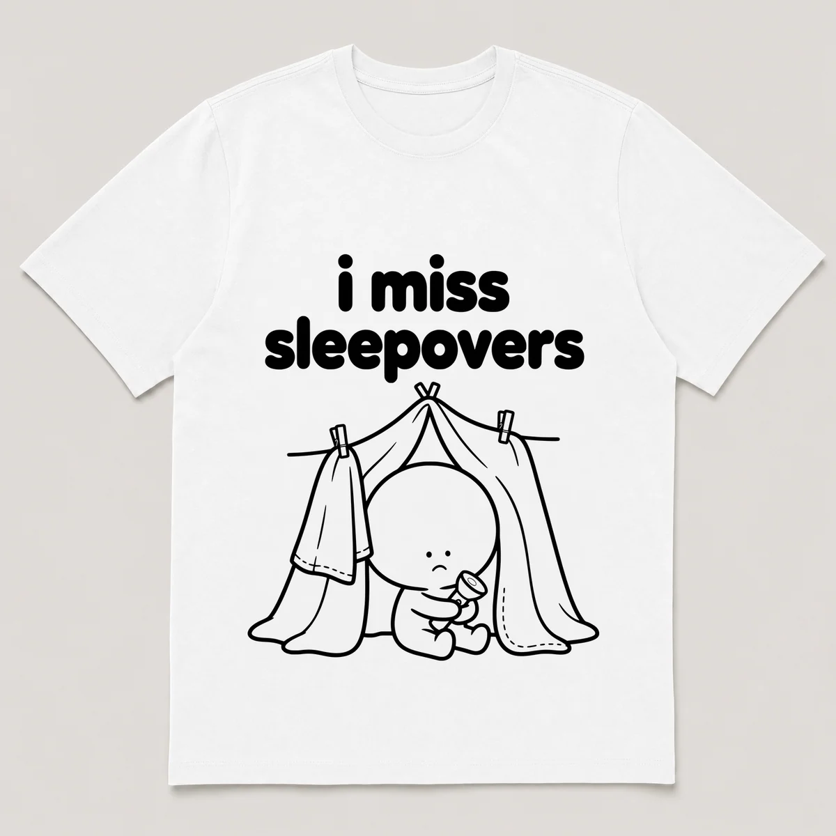 lonely boi tee: a small sad cartoon boy hugging a blanket fort with a flashlight, with the words i miss sleepovers above him, White front view